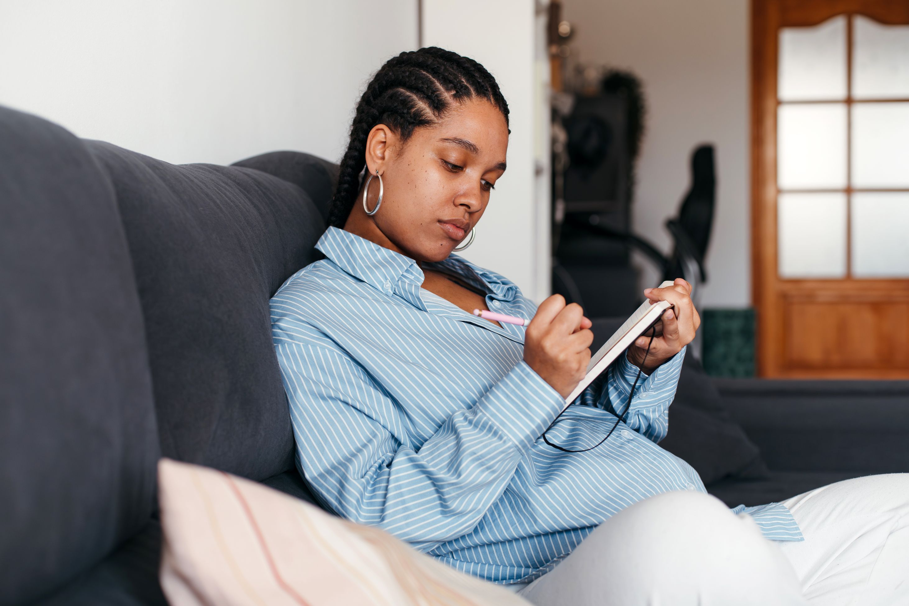 pregnant woman sitting on couch writing