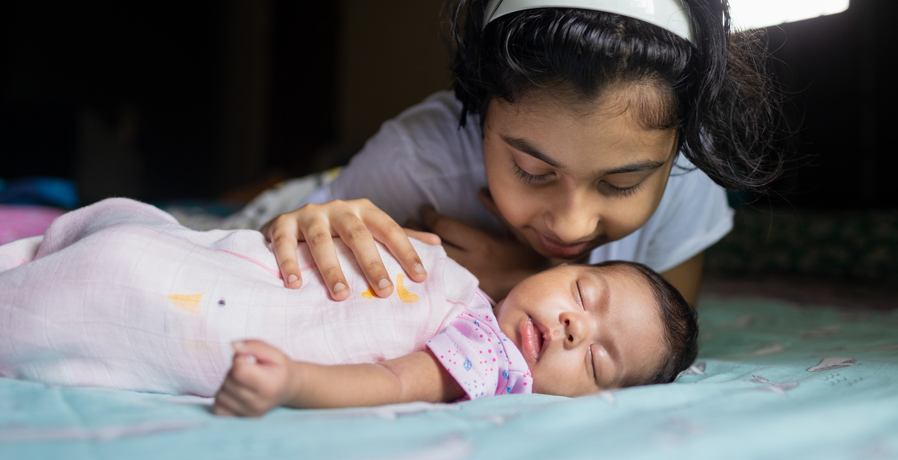 Girl cudding newborn baby sibling in bed