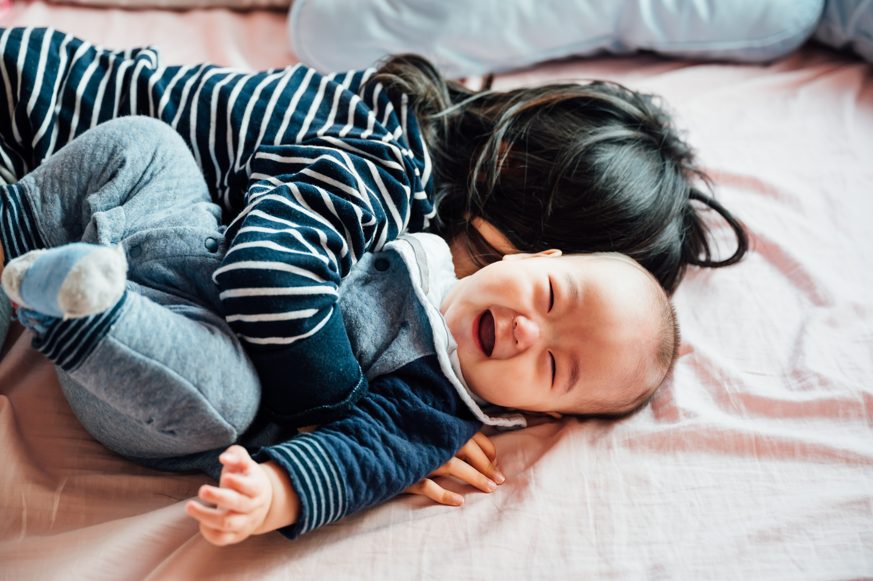 toddler and baby sibling playing on bed