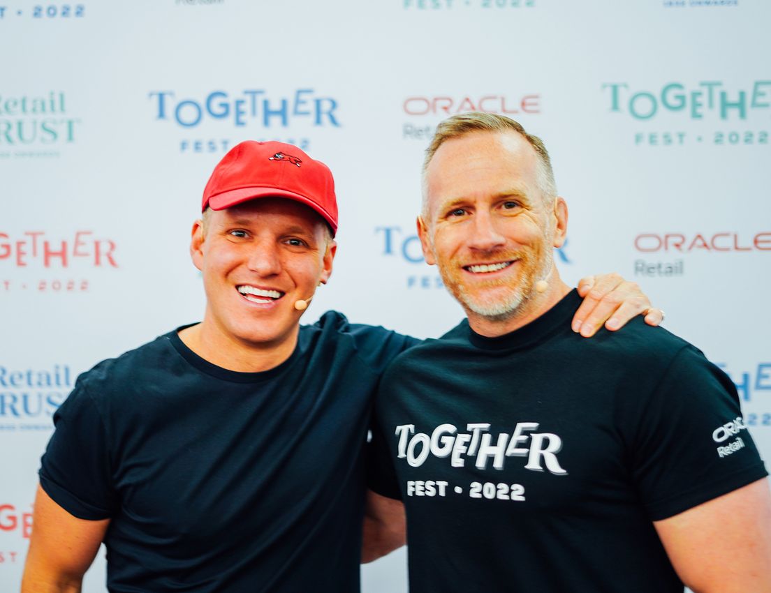 Two smiling men, one in a red cap, the other in a "Together Fest 2022" shirt, pose together against a branded backdrop.