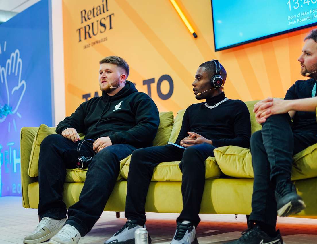 Three men on a lime green couch on a stage for a panel discussion. Two wear headphones with mics, one has headphones around h