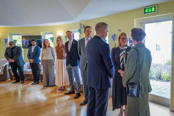 People in business attire form a reception line in a bright room with light wooden floors and celebratory bunting.