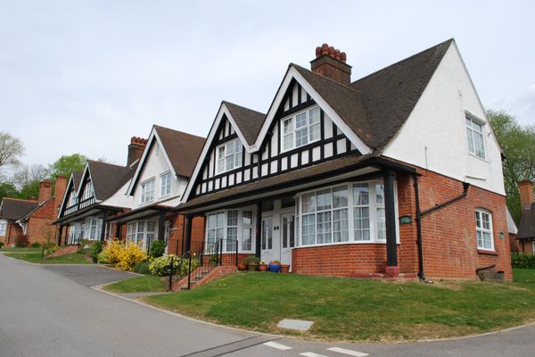 A row of traditional English houses with red brick, white stucco, and black timber framing, featuring gabled roofs and bay wi
