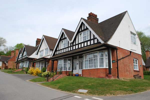 A row of traditional English houses with red brick, white stucco, and black timber framing, featuring gabled roofs and bay wi