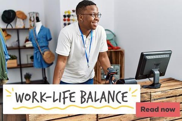 Smiling Black man with glasses working at a store counter with a monitor and scanner. Text overlay reads "WORK-LIFE BALANCE."