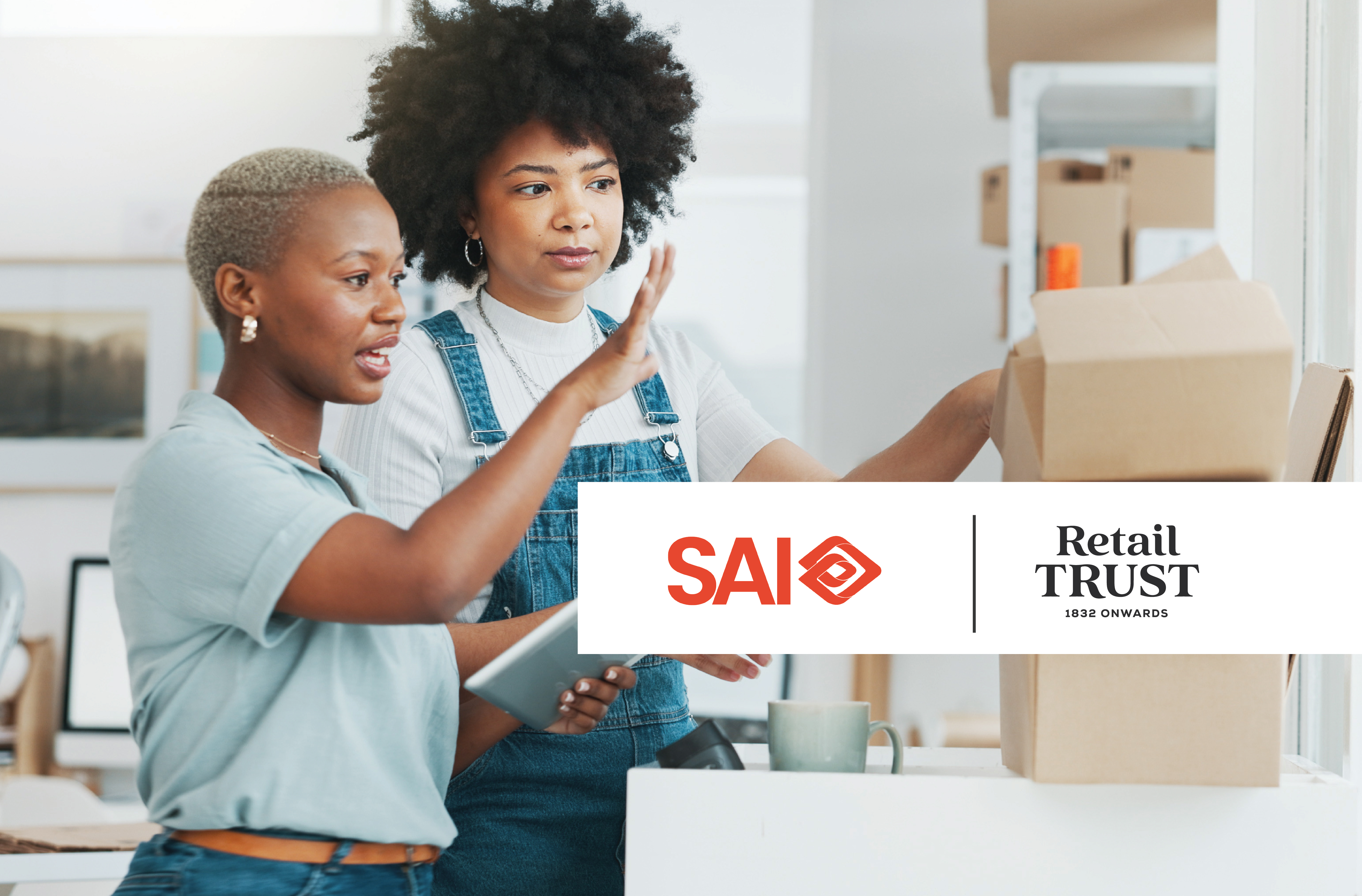 Two women collaborate, one with a tablet, packing cardboard boxes. Logos for SAI and Retail Trust overlay the scene.