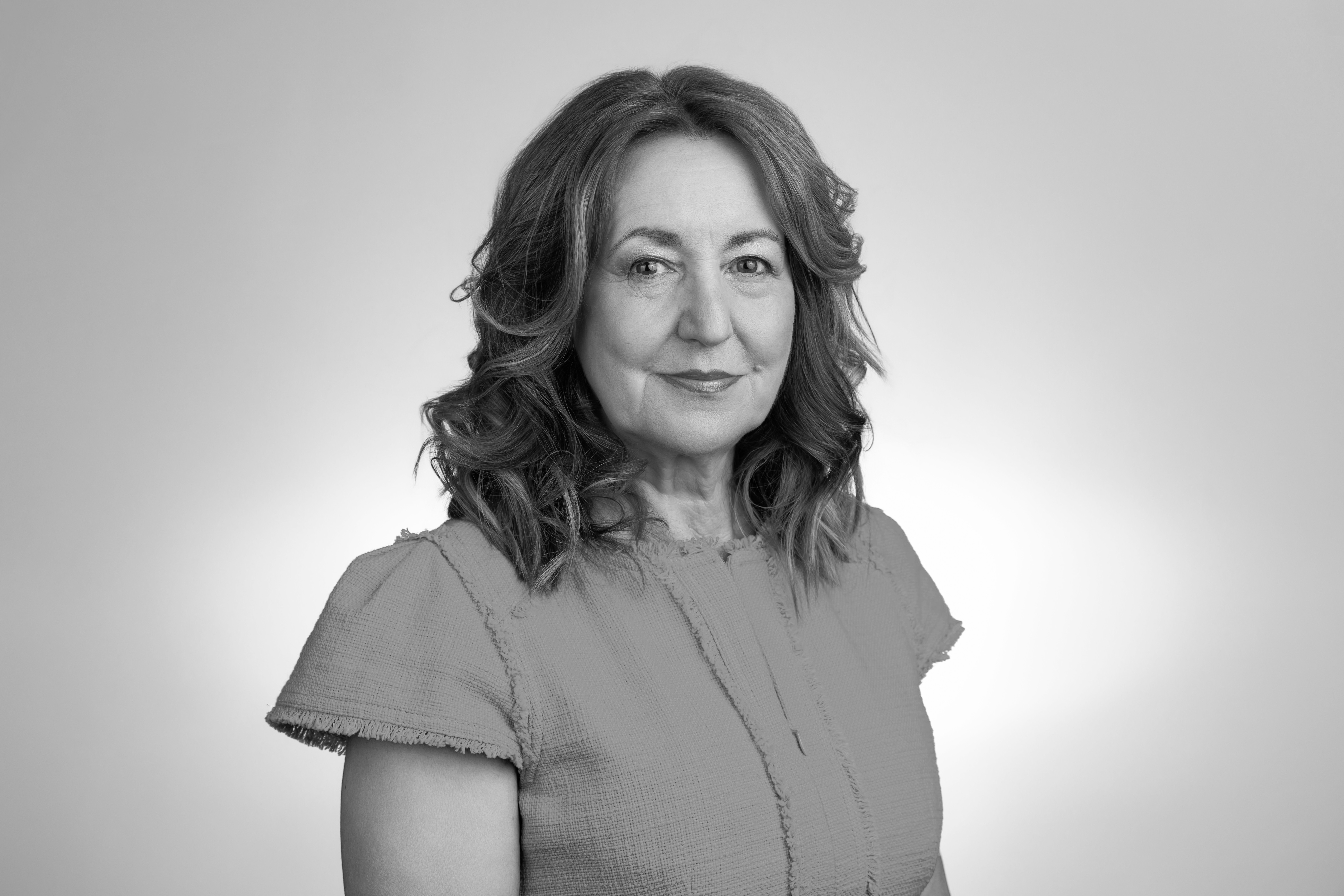 Black and white headshot of a smiling middle-aged woman with curly hair wearing a textured top against a light background.