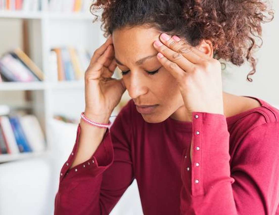 A woman in a red sweater sits with eyes closed, pressing her temples with her fingers, appearing to have a headache. Bookshel