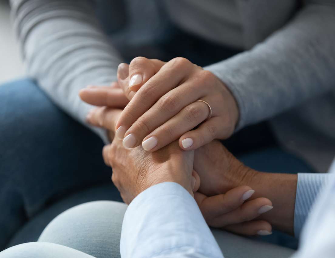 Close-up of two hands, one wearing a ring, clasped together to offer comfort, empathy, and emotional support.