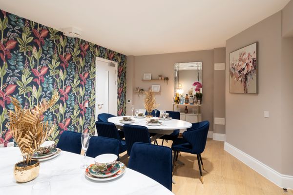 Elegant dining room with a floral-feature wall, blue chairs, set dining table, and a side table with decor and mirror.