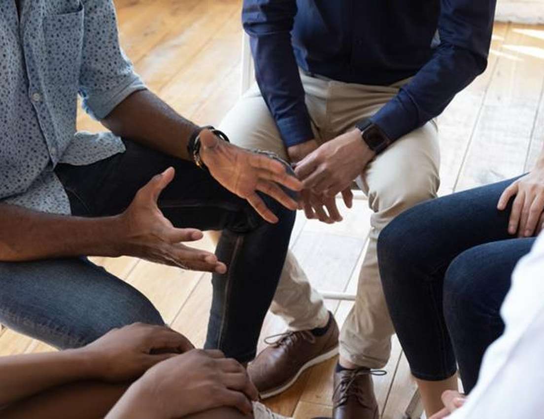Close-up of people sitting in a circle, with hands gesturing, engaged in a discussion or meeting.