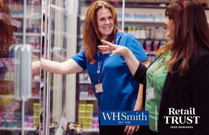 Smiling WHSmith employee helps a customer, opening a refrigerated display in a store.