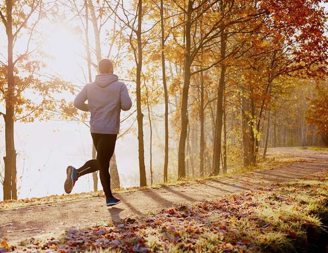 A person jogs on a frosty autumn path by a misty lake, surrounded by trees with golden leaves and bright morning sun.