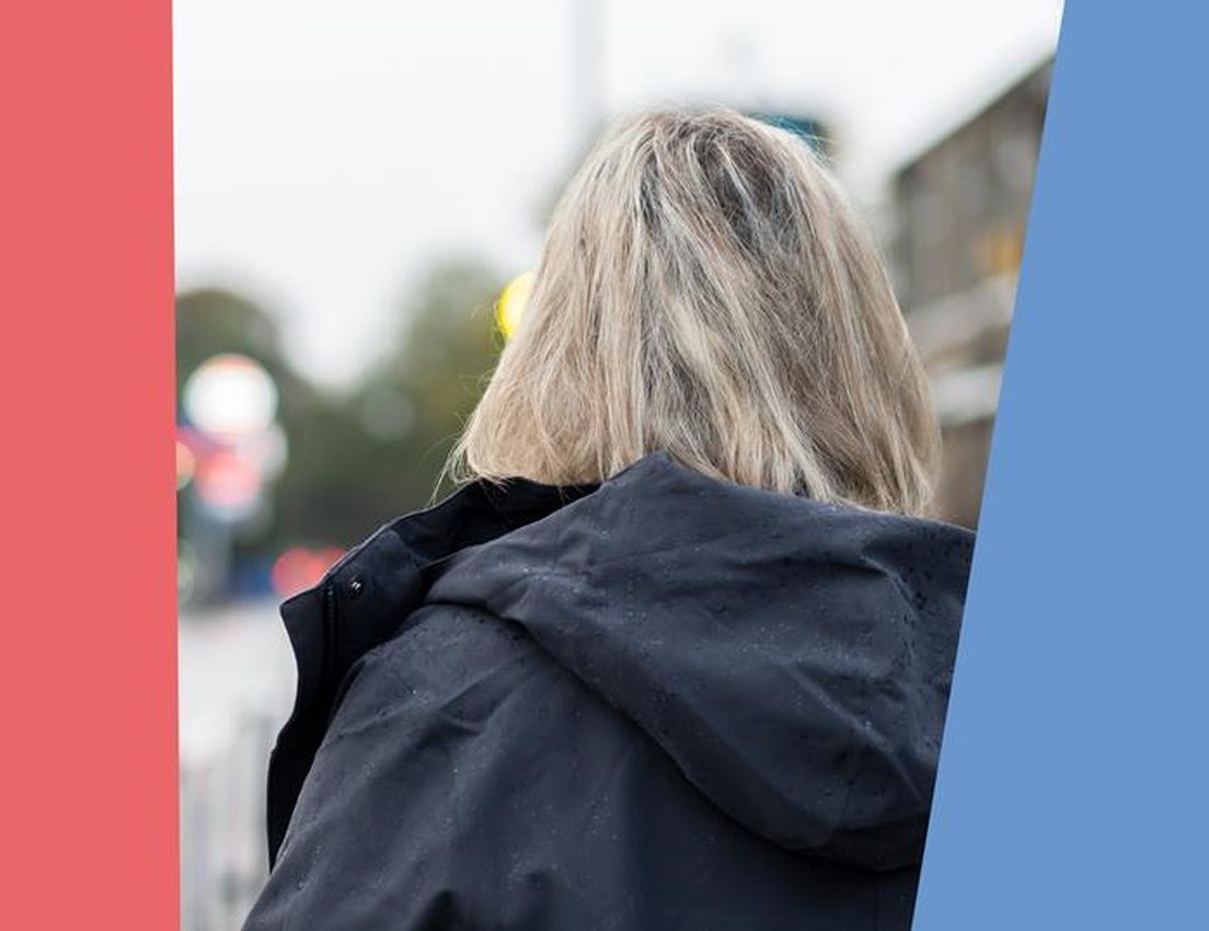 Raindrops on a dark blue waterproof jacket worn by a person with blonde hair, walking outdoors with a blurred street backgrou