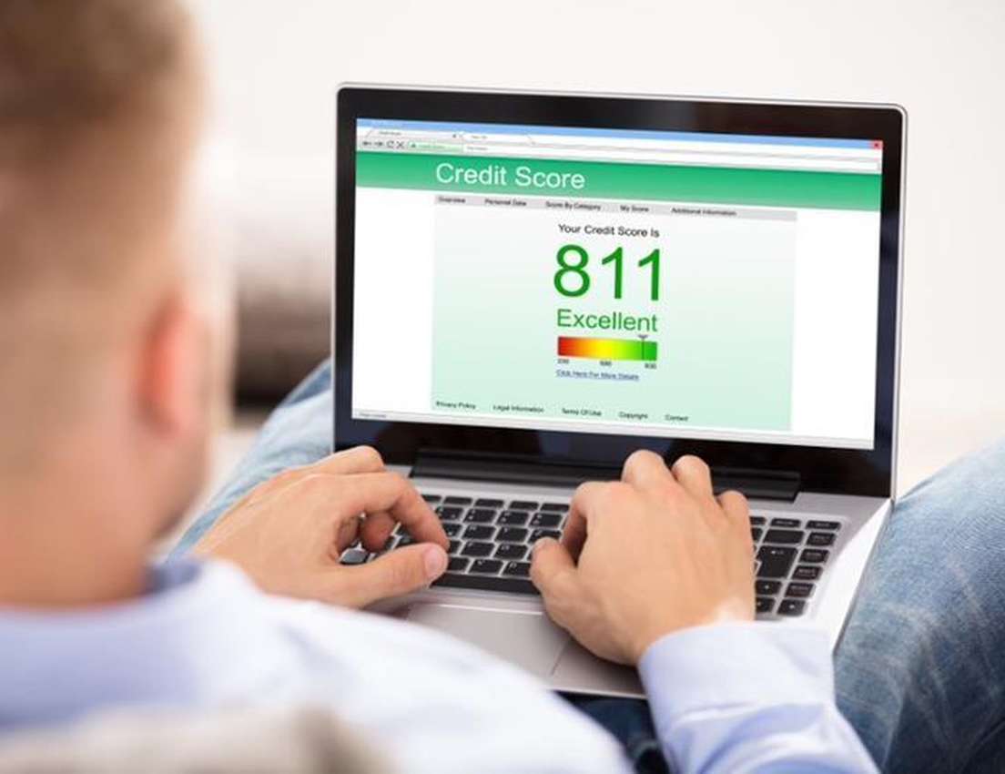 A person views an "Excellent" credit score of 811 on a laptop screen, typing on the keyboard.