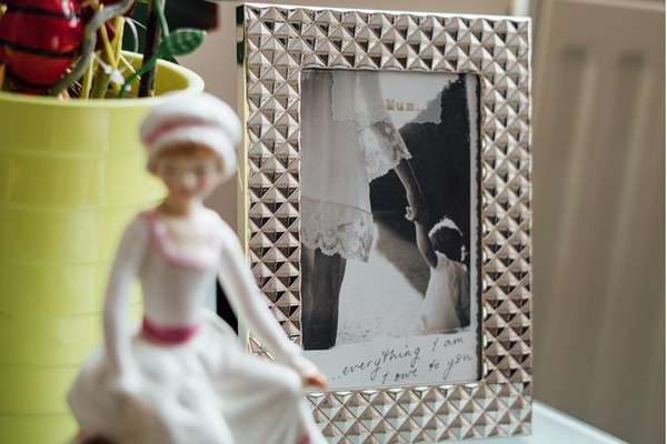 A silver studded frame displays a black and white photo of a mother and child holding hands. Text reads "Mum..." and "...everything I am I owe to you".