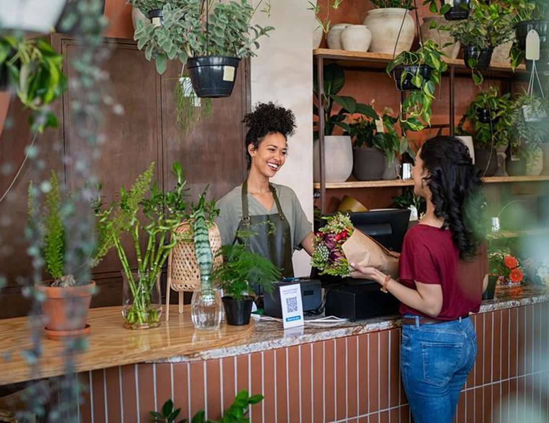 Smiling employee hands wrapped flowers to a customer in a vibrant plant shop.