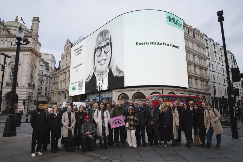 Group poses at Piccadilly Circus, London, with a large billboard showing a smiling woman and text 'Every smile is a stand', promoting 'Let's Respect Retail'.