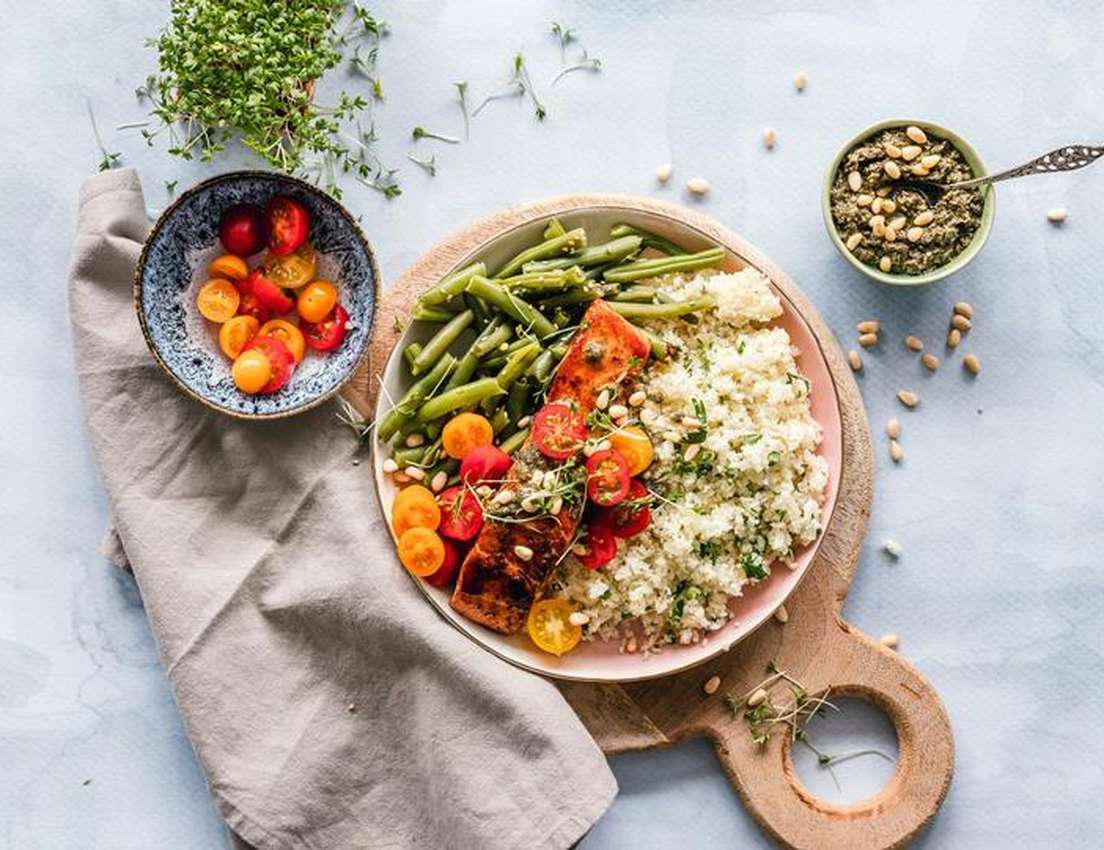 Overhead view: a healthy meal of grilled salmon, green beans, quinoa, and cherry tomatoes, with pesto & pine nuts, on a woode