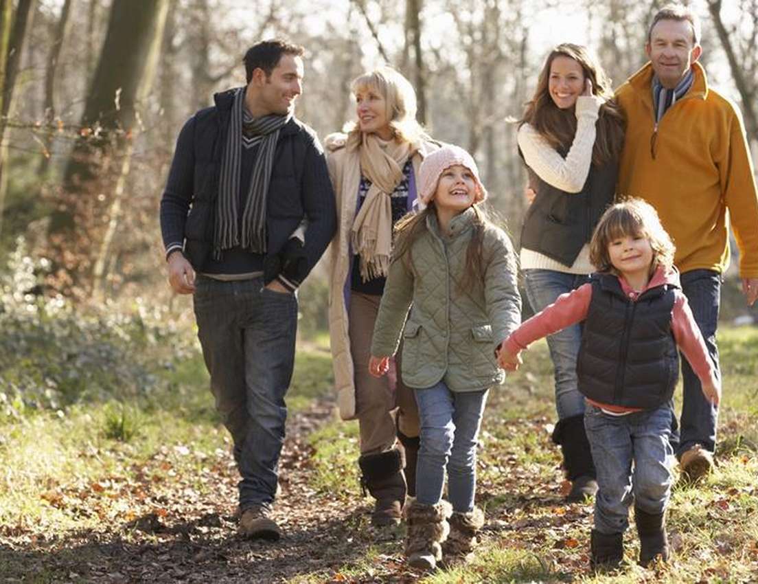 A happy multi-generational family of six, including children, parents, and grandparents, walks through a sunny, autumn park.