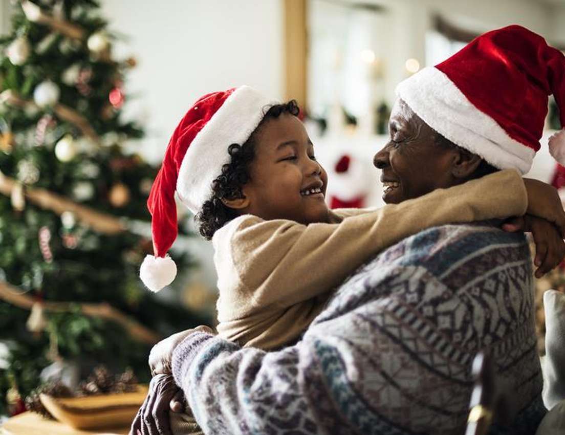 Happy grandmother and child in Santa hats hugging by a Christmas tree.