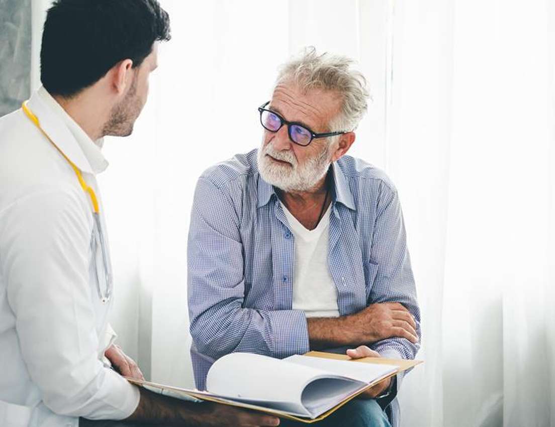 Doctor consulting with an elderly man, reviewing documents together in a well-lit room.