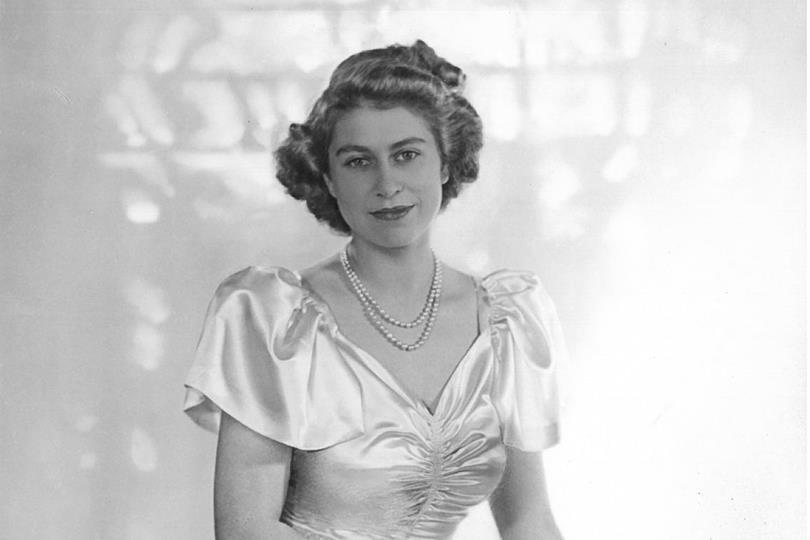 Black and white portrait of young Queen Elizabeth II in a satin dress with puffed sleeves, double pearl necklace, and a slight smile.