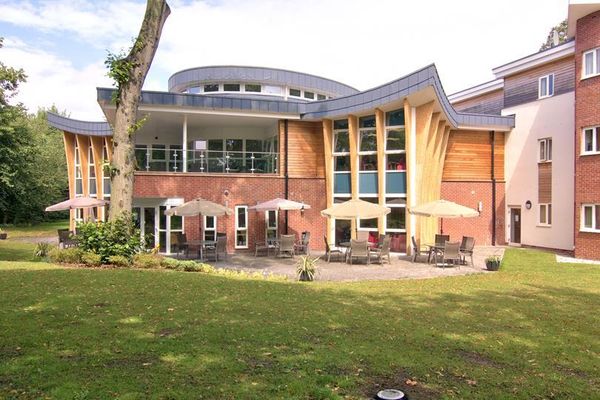 Modern building with curved roof and wood panel accents, featuring patio tables and umbrellas on a grassy area surrounded by