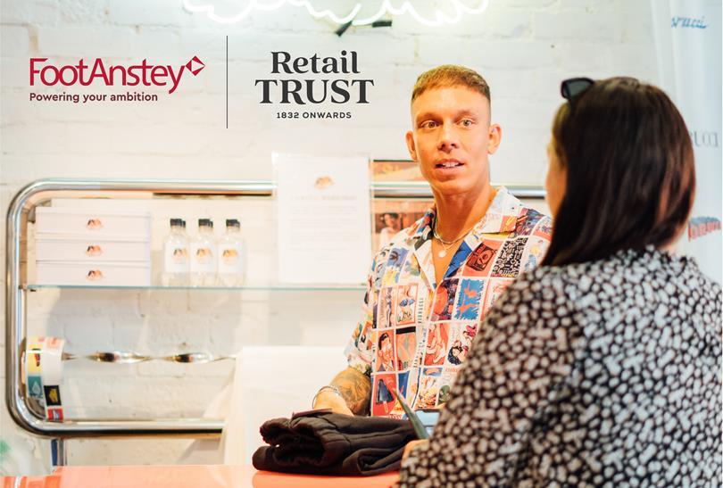 A man in a colorful patterned shirt speaks to a woman at a retail counter. FootAnstey and Retail Trust logos are displayed.