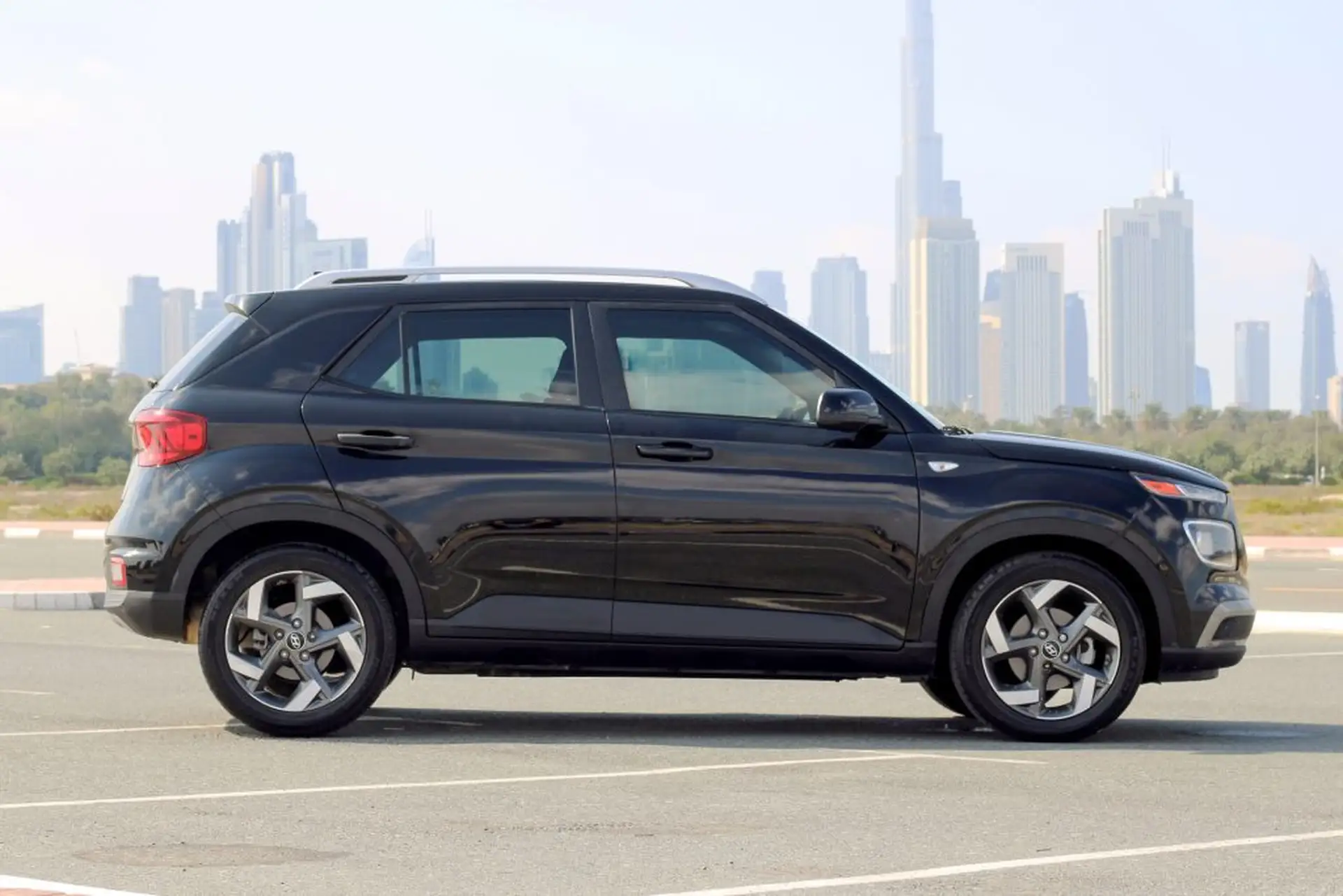 Black SUV parked in an open lot with a city skyline in the background under a clear sky.