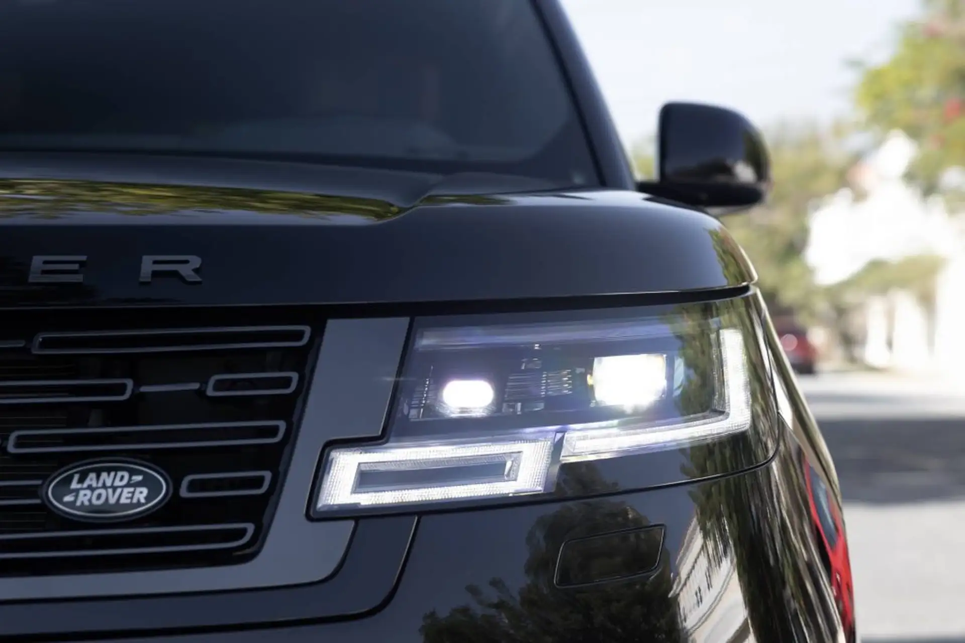Close-up of a black Land Rover vehicle with focus on its modern LED headlights and grille, parked on a street with blurred background.