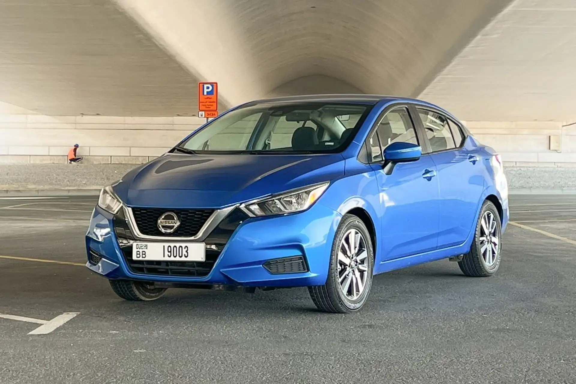 A blue sedan parked under a concrete structure. It's a modern car with a sleek design and visible alloy wheels.