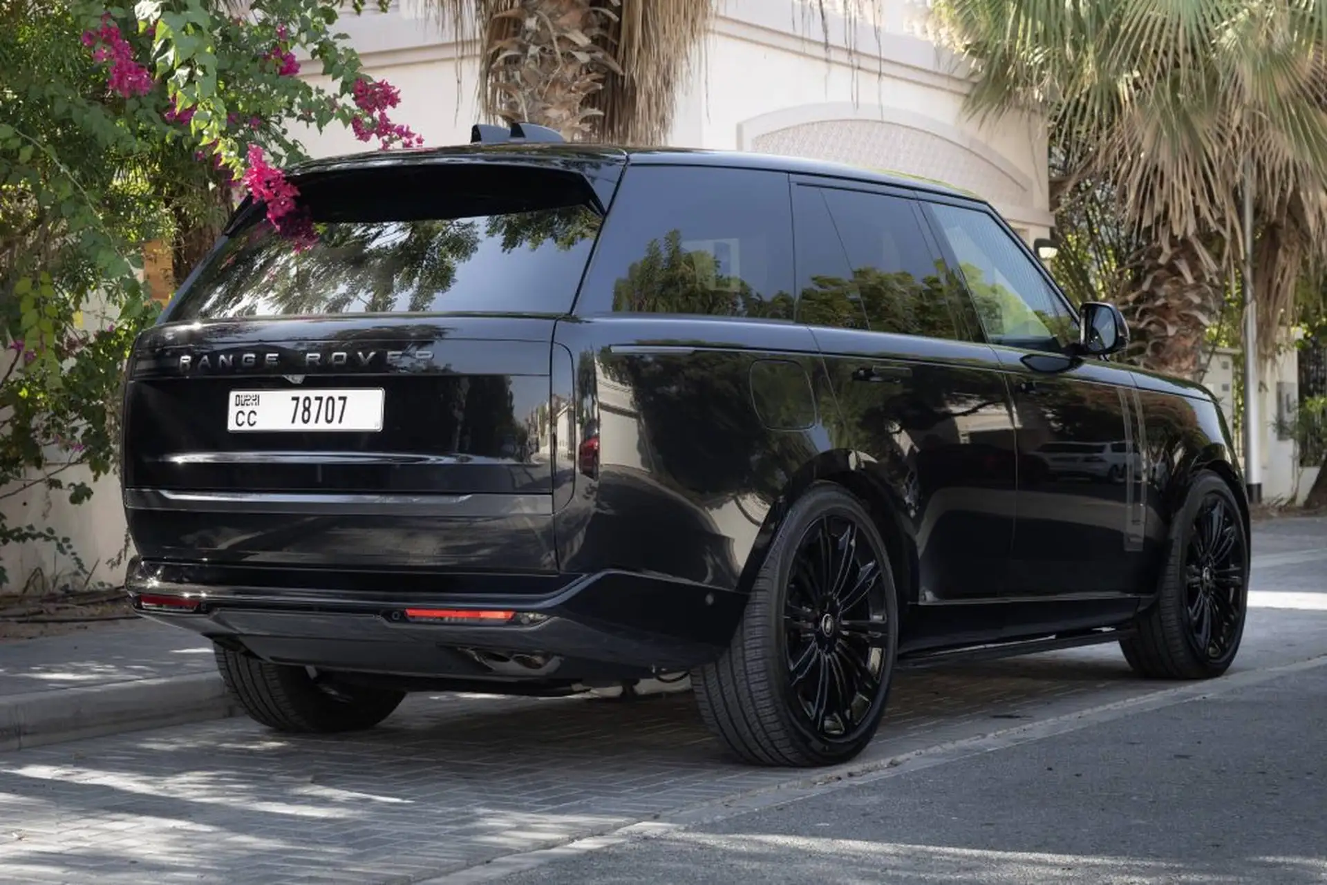 Black Range Rover parked on a street, surrounded by lush greenery and palm trees. Dubai license plate visible.