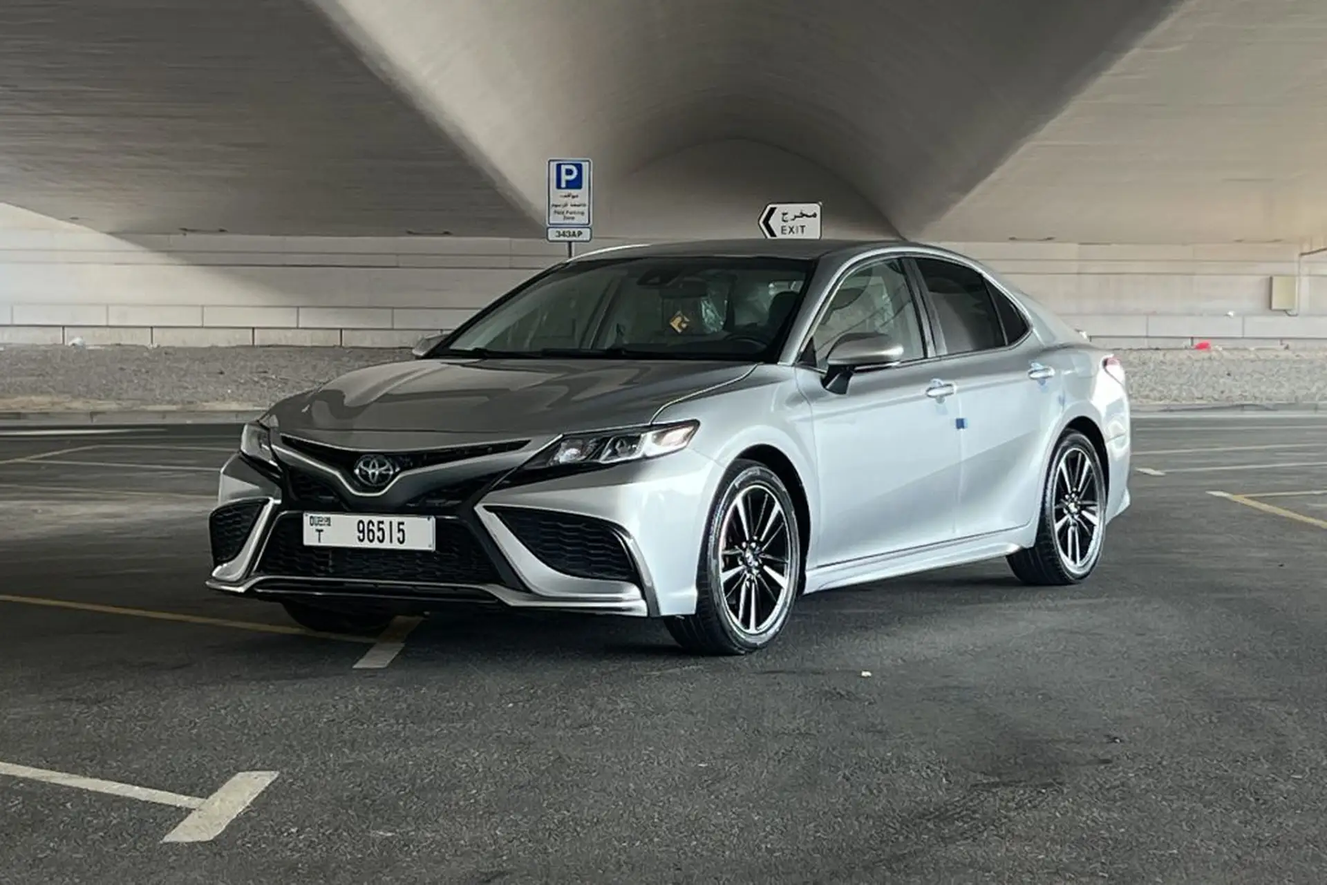Silver Toyota sedan parked in a spacious, covered parking area with directional signs and a parking meter nearby.