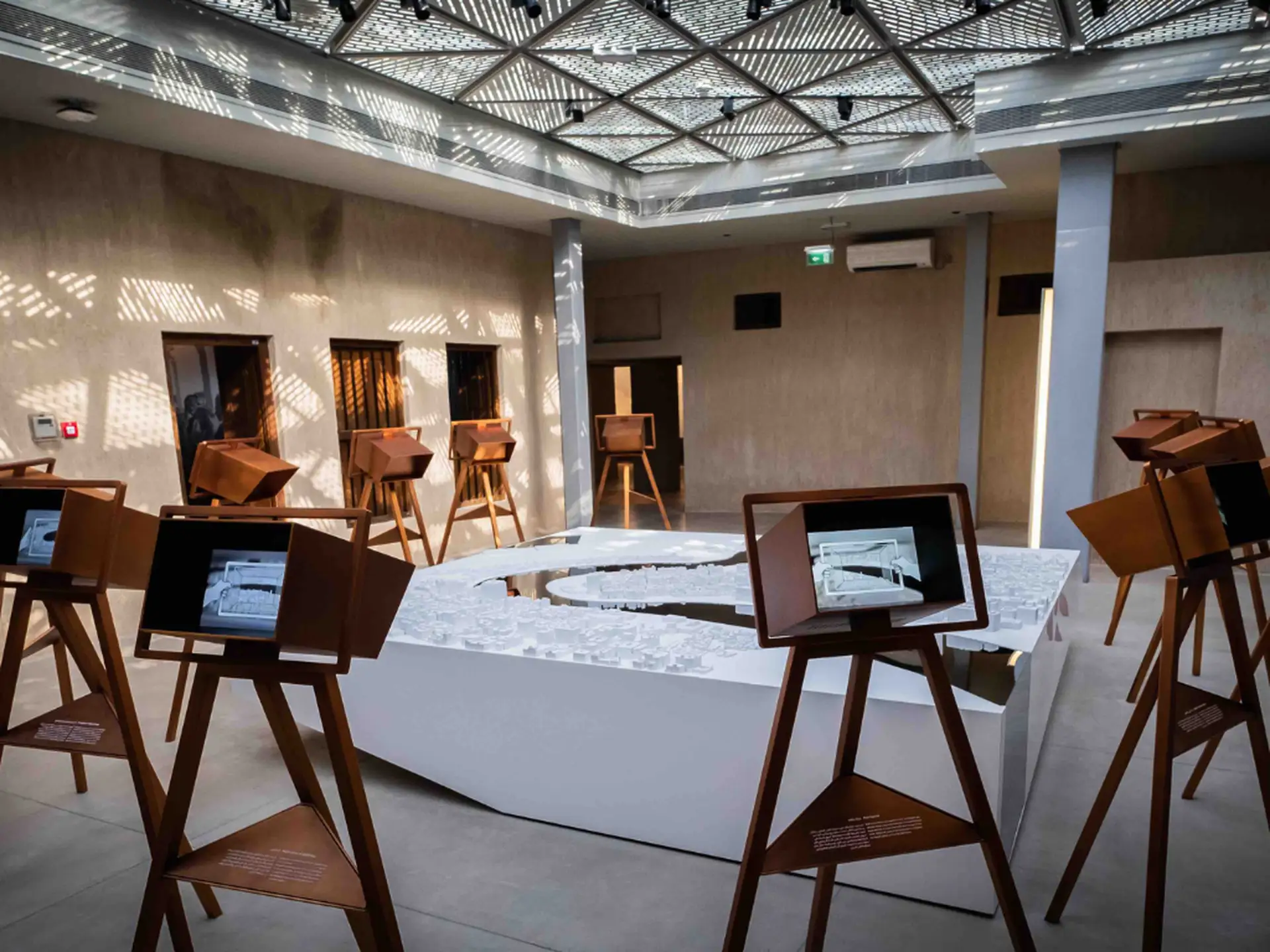 Art exhibit with tablets on easels surrounding a central white sculpture in a modern, well-lit room with patterned ceiling lights.