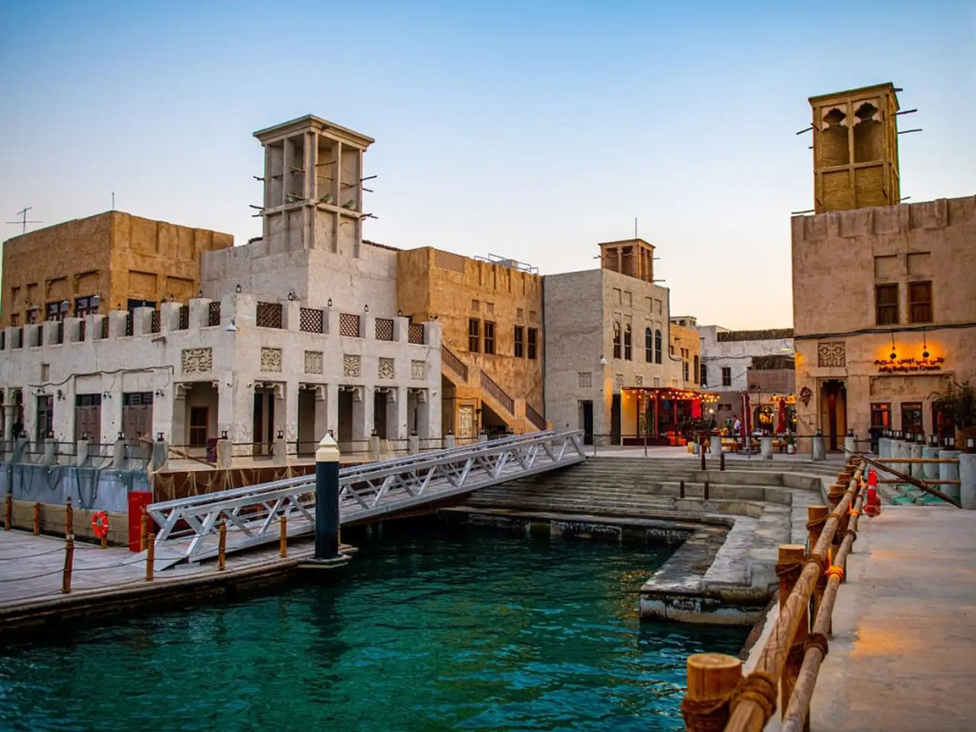 A serene canal bordered by traditional Middle Eastern architecture at sunset, featuring wind towers and adorned buildings.