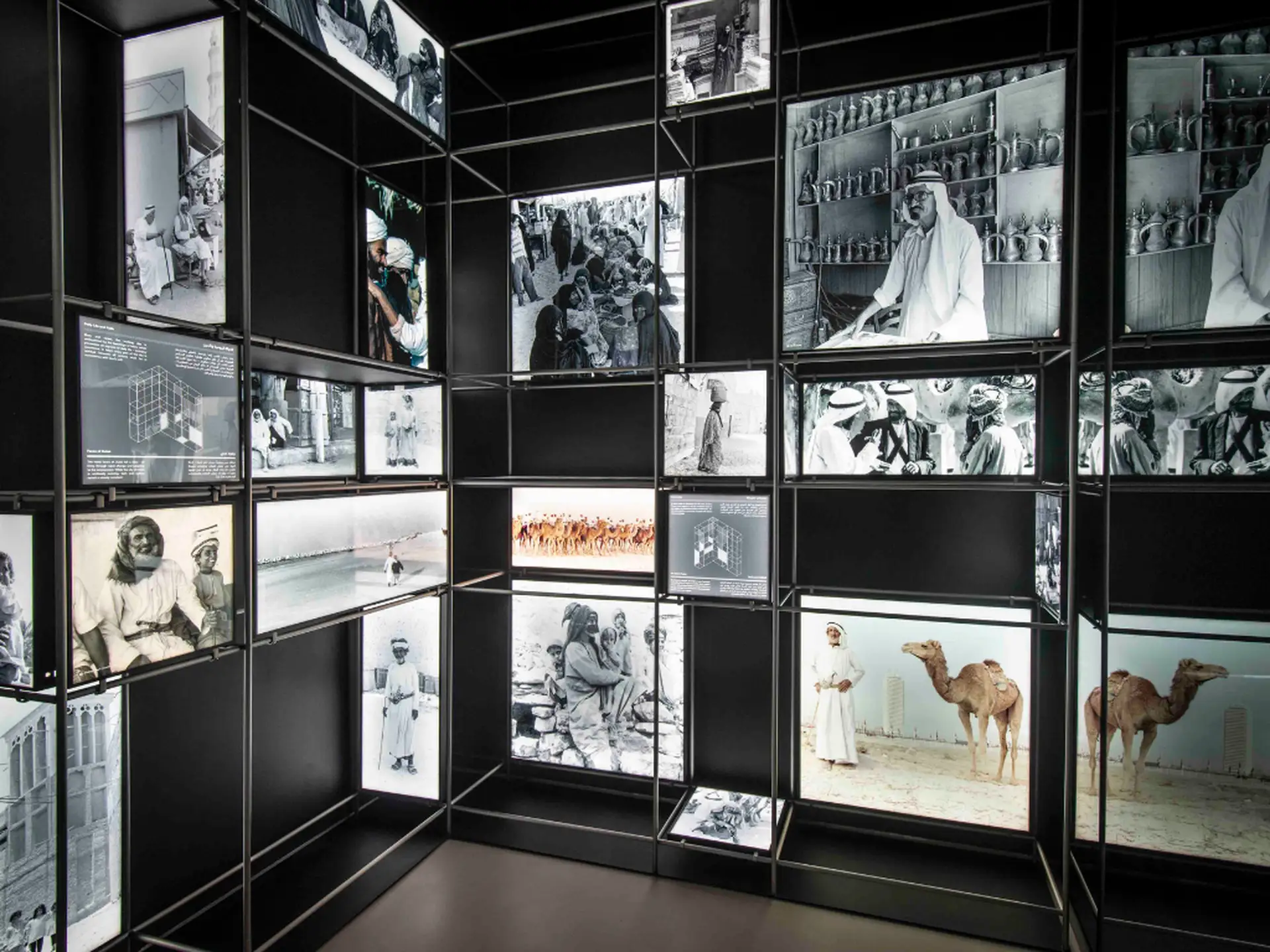 A wall display of historical black-and-white photos and artifacts, including camels and people in traditional attire, in a well-lit exhibit.