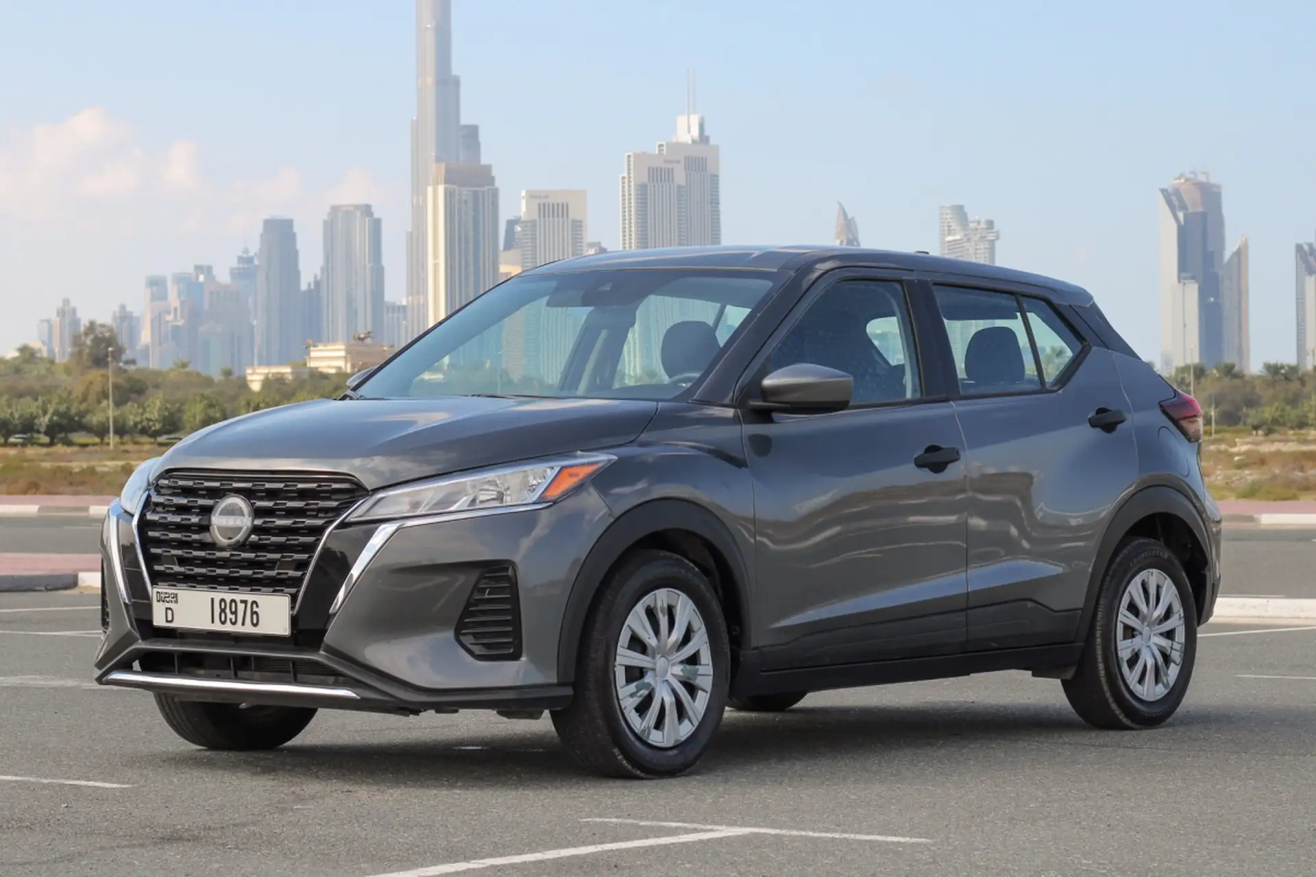 Gray Nissan SUV parked on a road with a city skyline in the background under a clear blue sky.