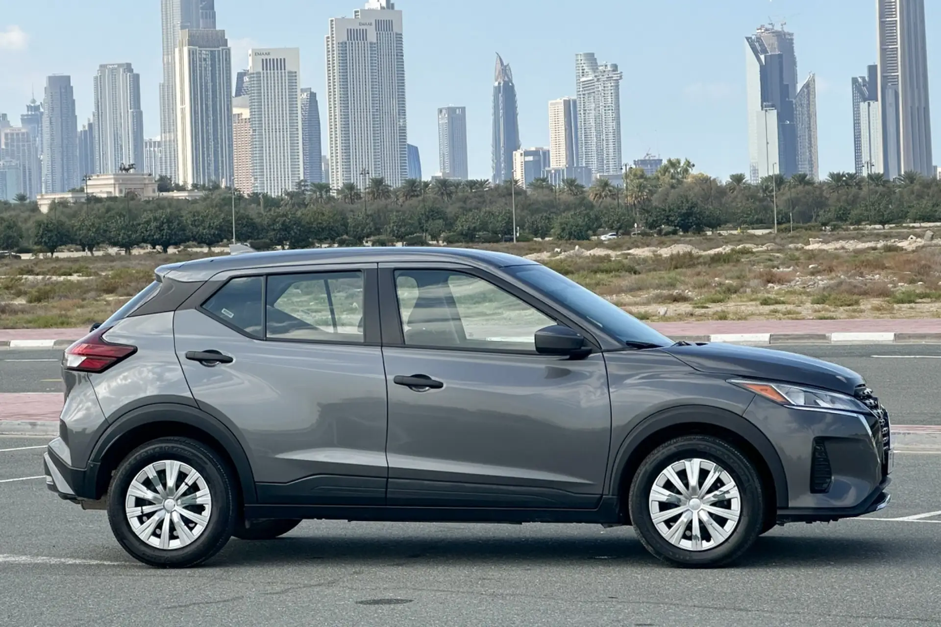 A gray SUV parked on a road with a city skyline in the background under a clear sky.
