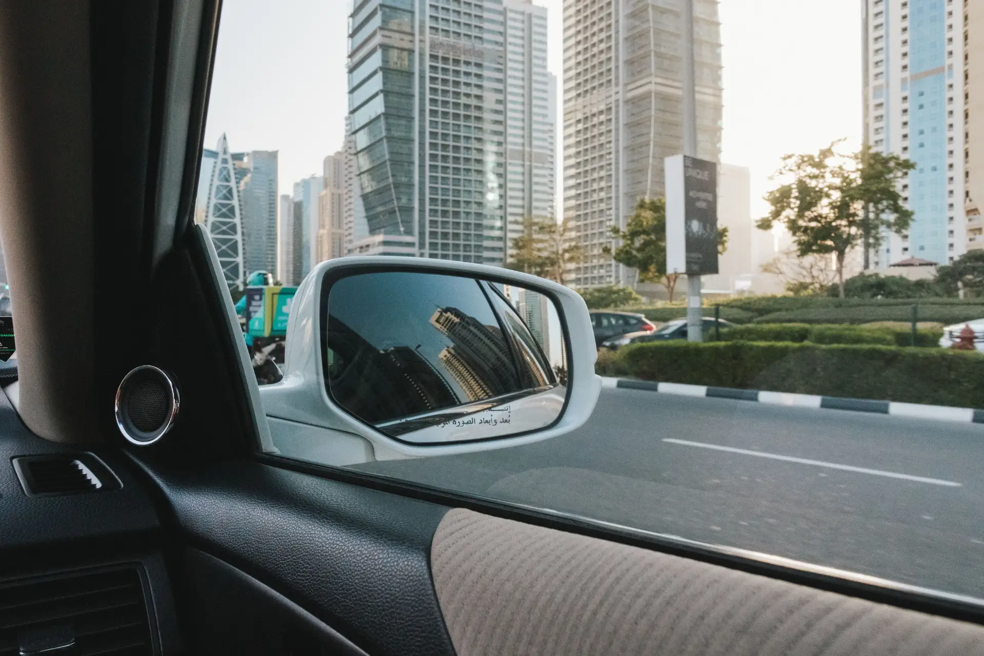 A view from inside a car focuses on the side mirror reflecting a skyline of modern skyscrapers.