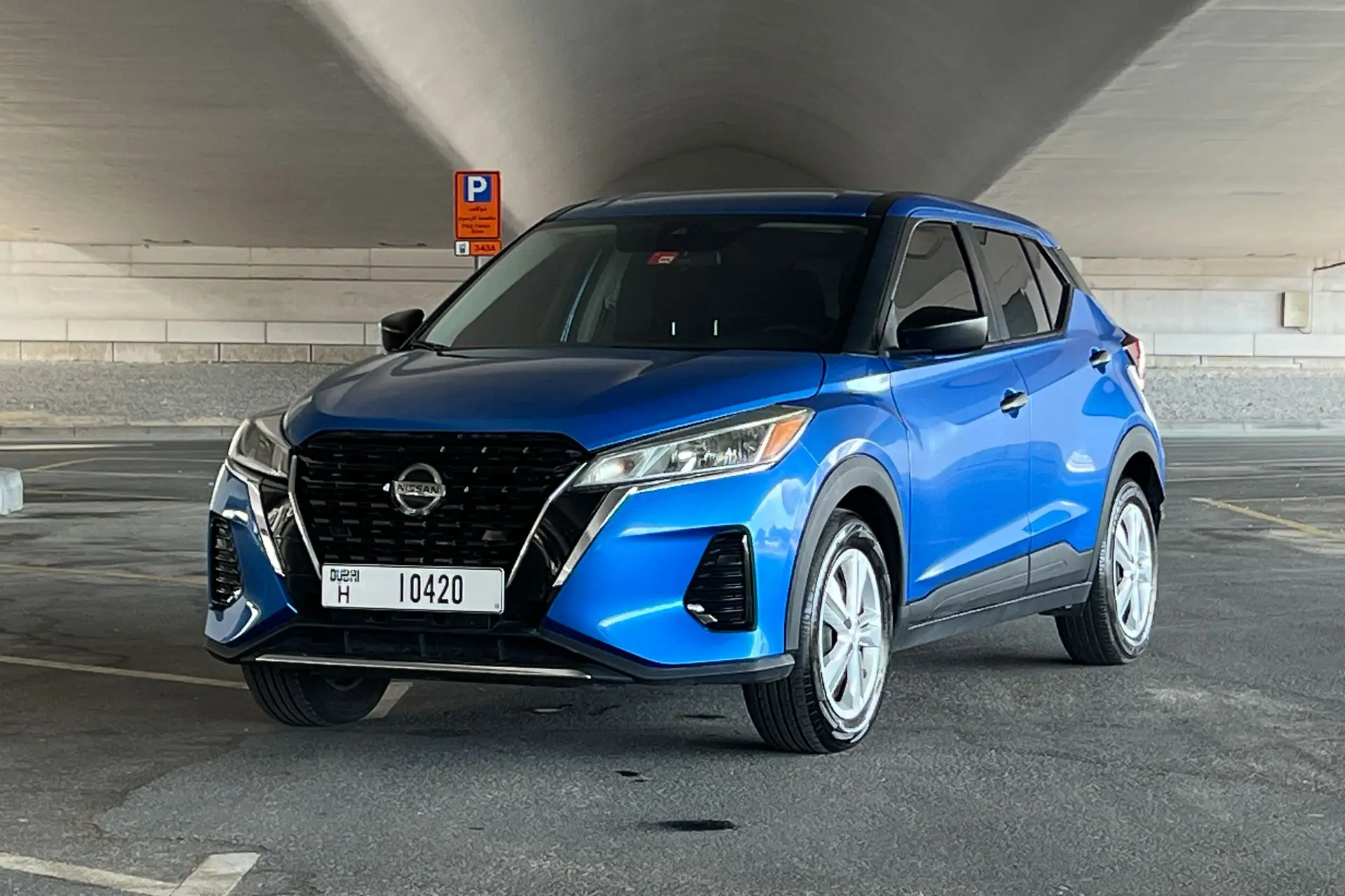 A blue Nissan SUV parked in a covered lot with visible parking lines and a parking sign in the background.