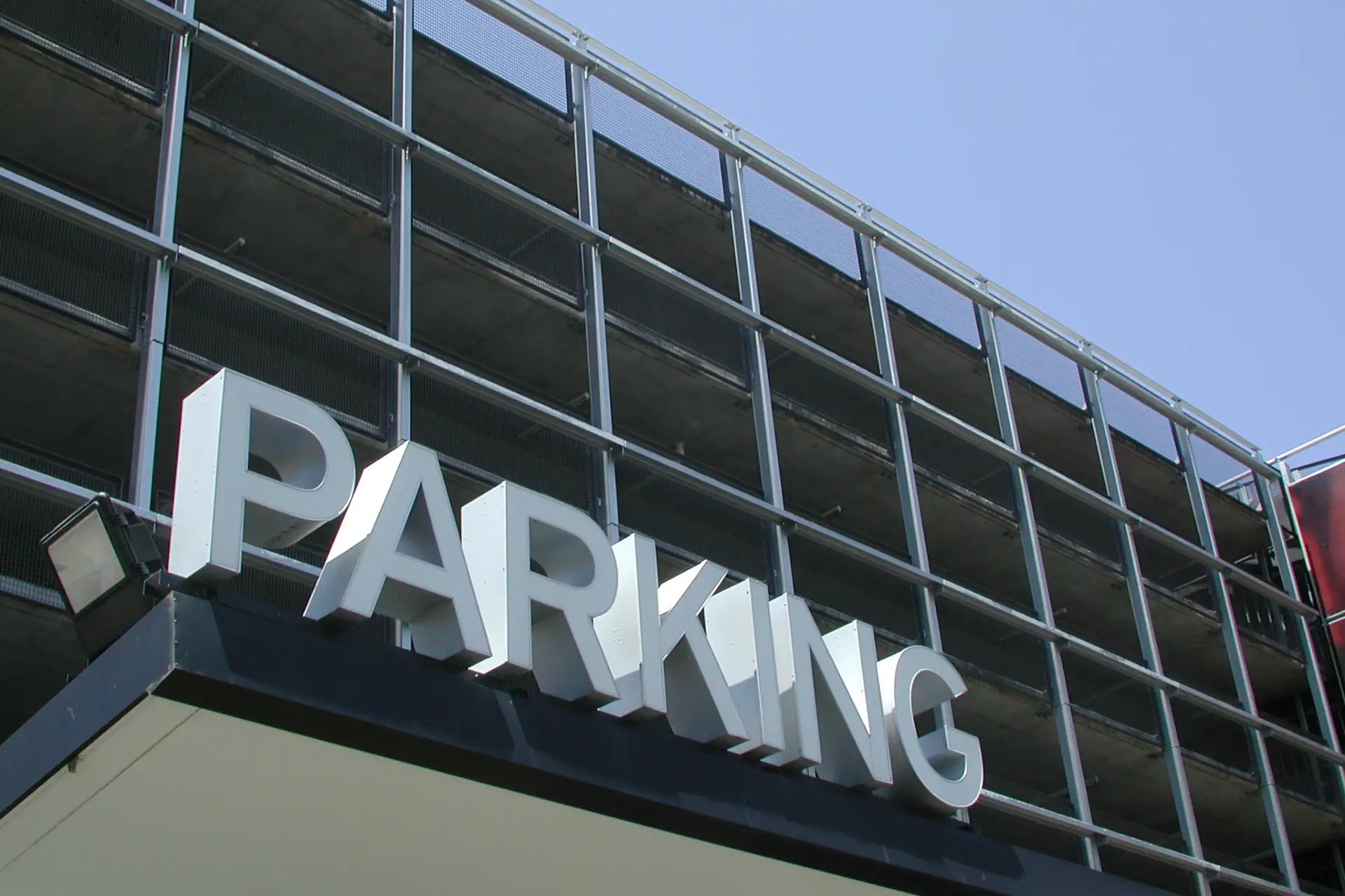 A large sign with the word "PARKING" is mounted on a building with a grid-like facade under a clear blue sky.