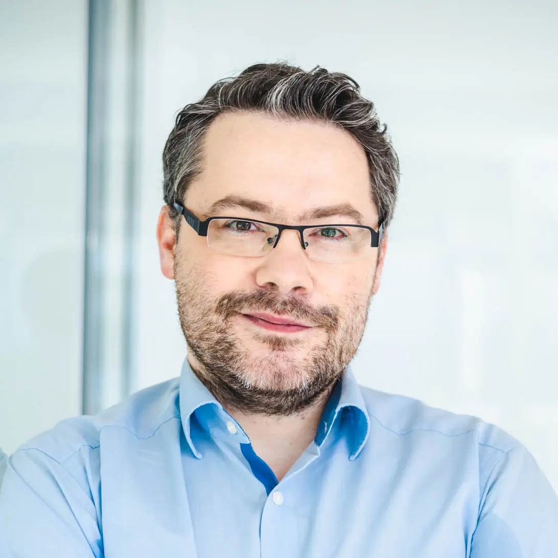 Man with glasses and a beard wearing a blue shirt.