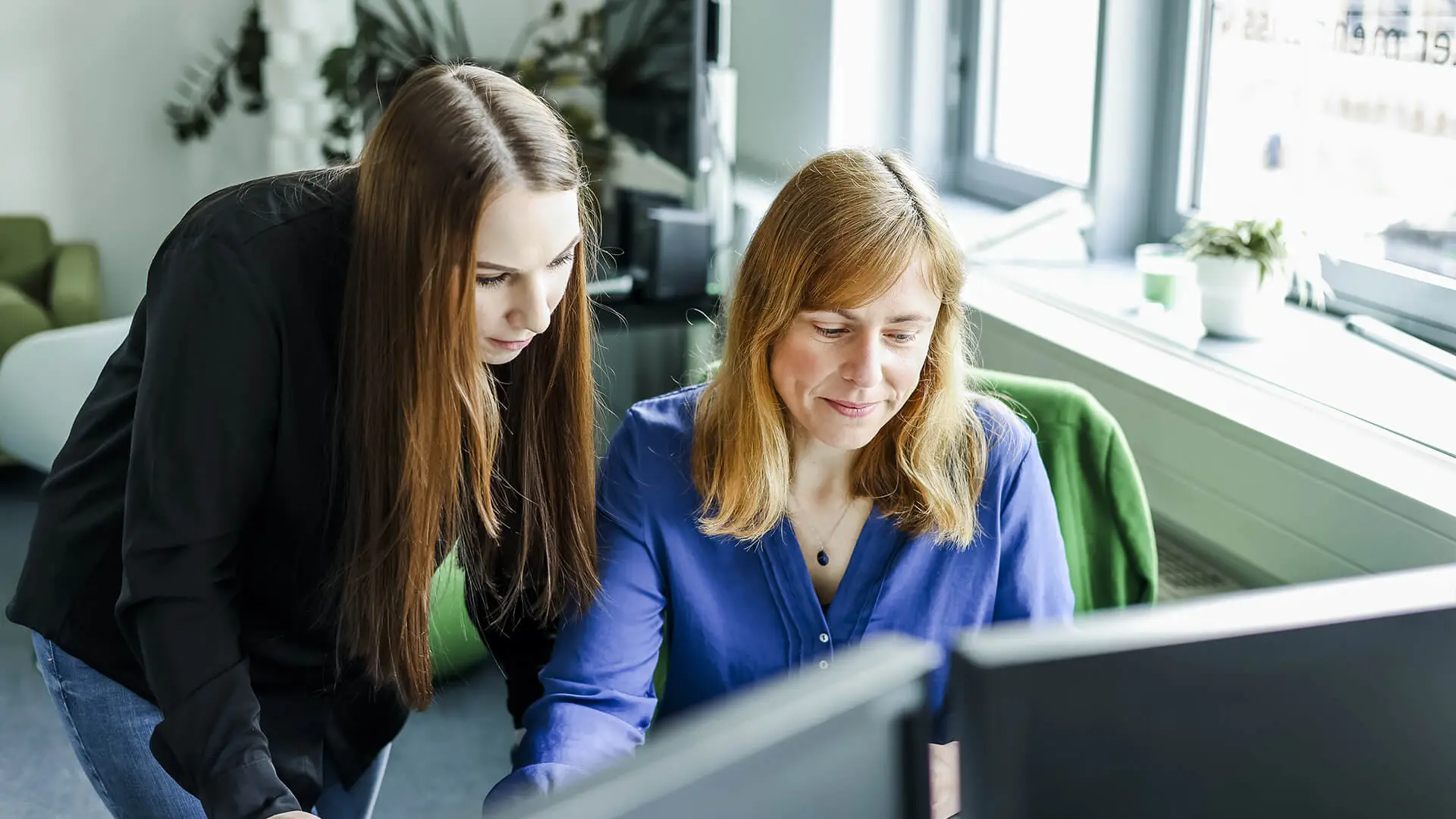 Two women in an office, one standing and one seated.