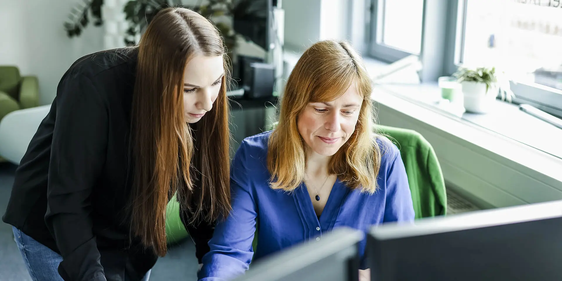Two women in an office, one standing and one seated.