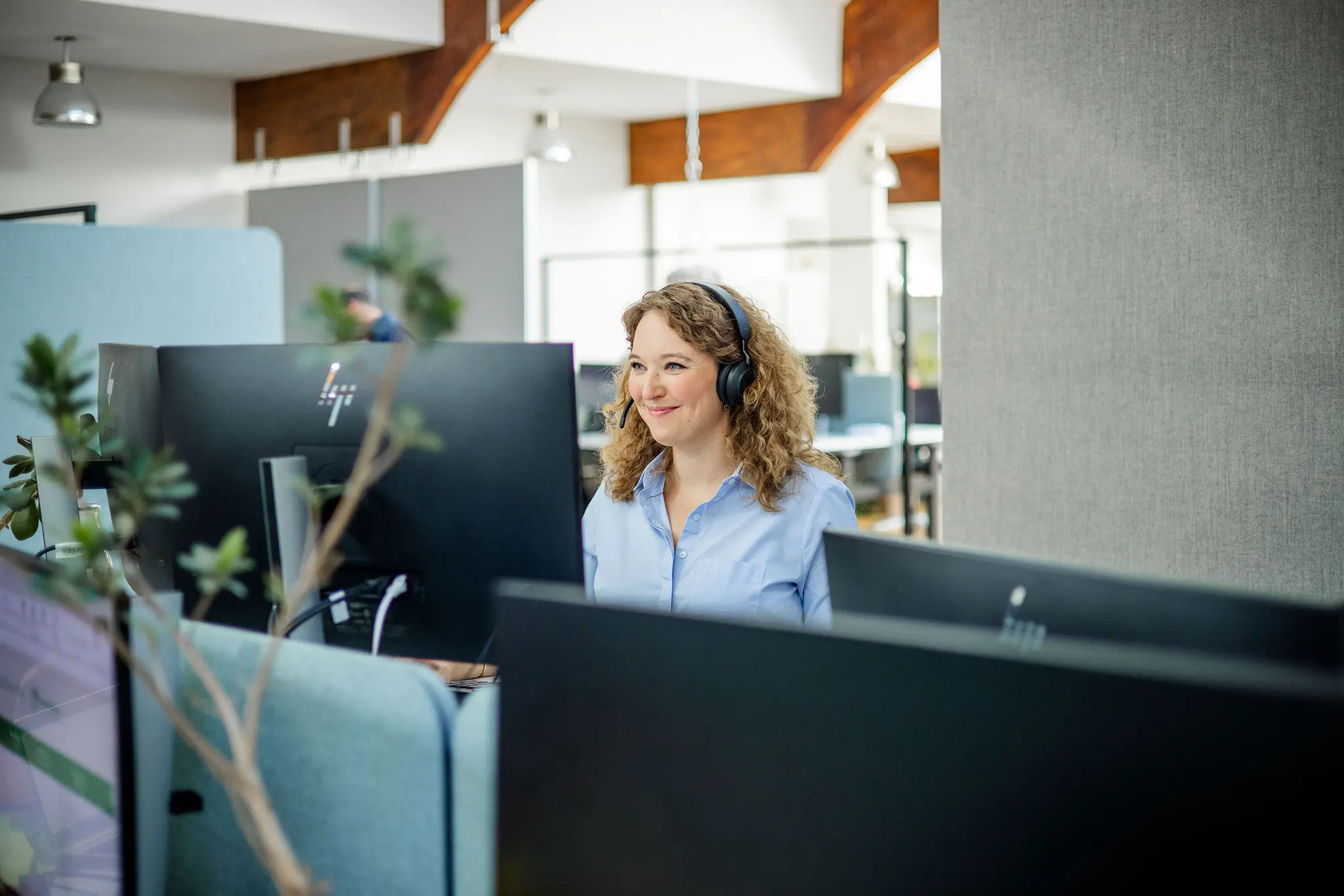 Woman with curly hair and headset smiling while working at a computer.