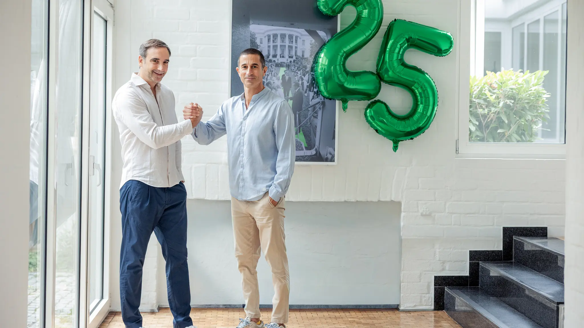 Jens Schmitz und Fady El-Murr geben sich die Hand vor einer grünen Ballonzahl 25