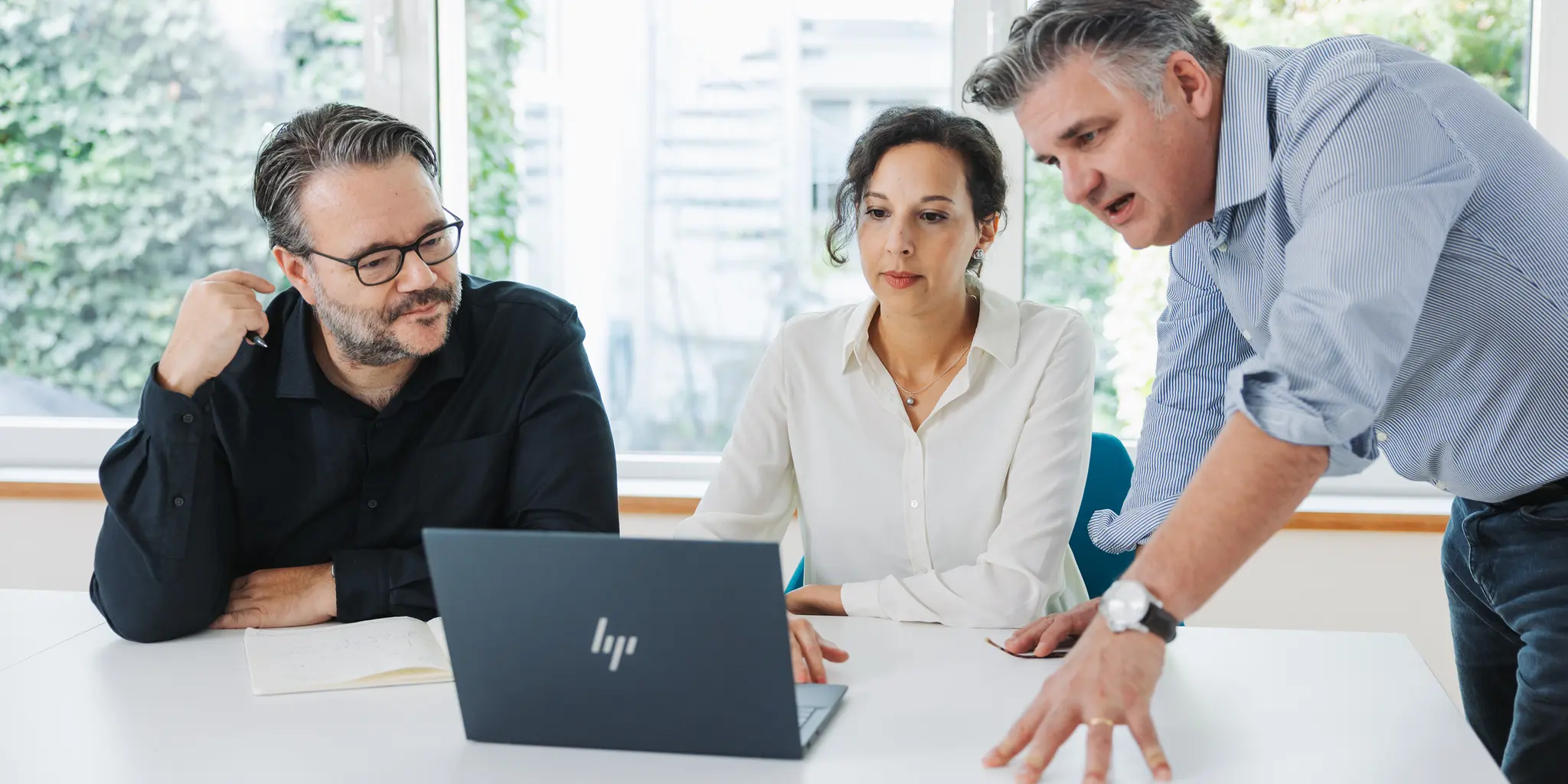 Three people in a meeting, focused on a laptop screen.