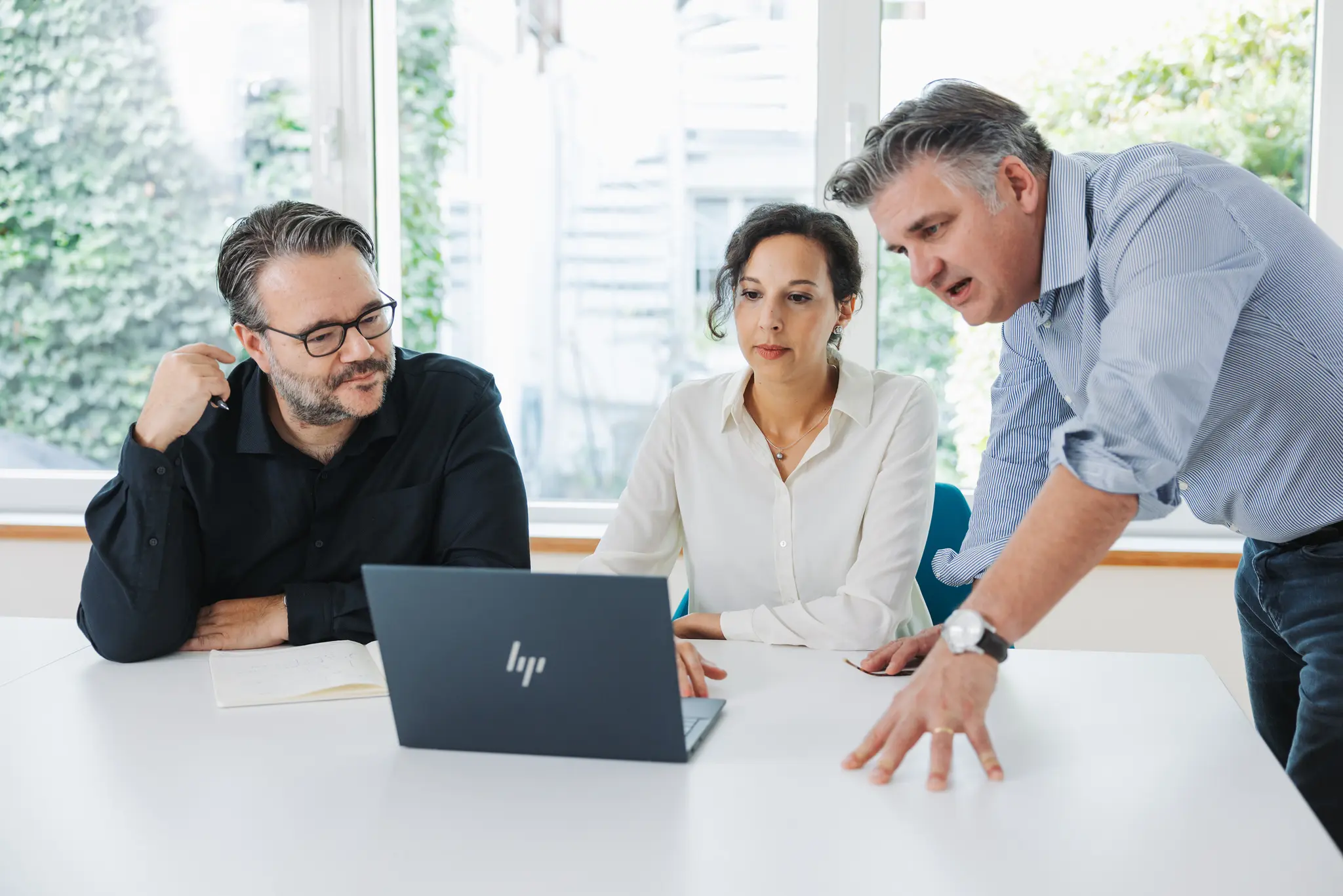 Three people discussing at a table with a laptop.