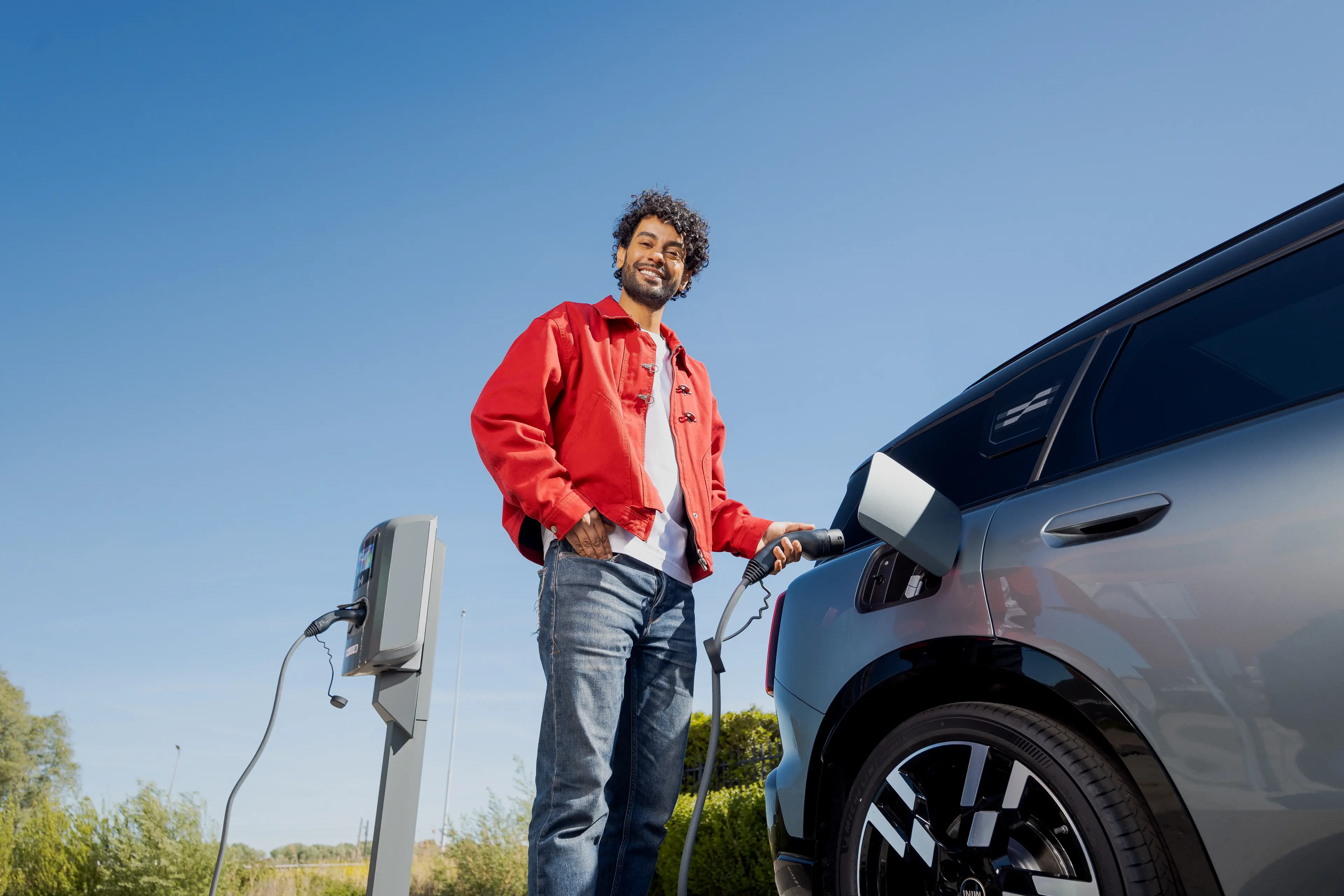 Man in een rood jack laadt zijn elektrische auto bij een laadpaal